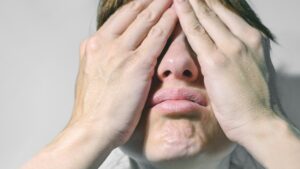 Closeup of beautiful young woman isolated on gray background covering her face