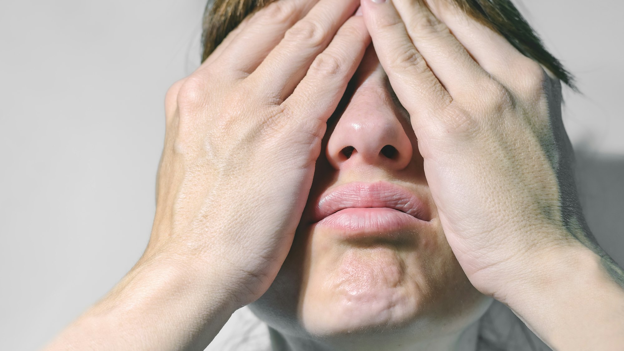 Closeup of beautiful young woman isolated on gray background covering her face