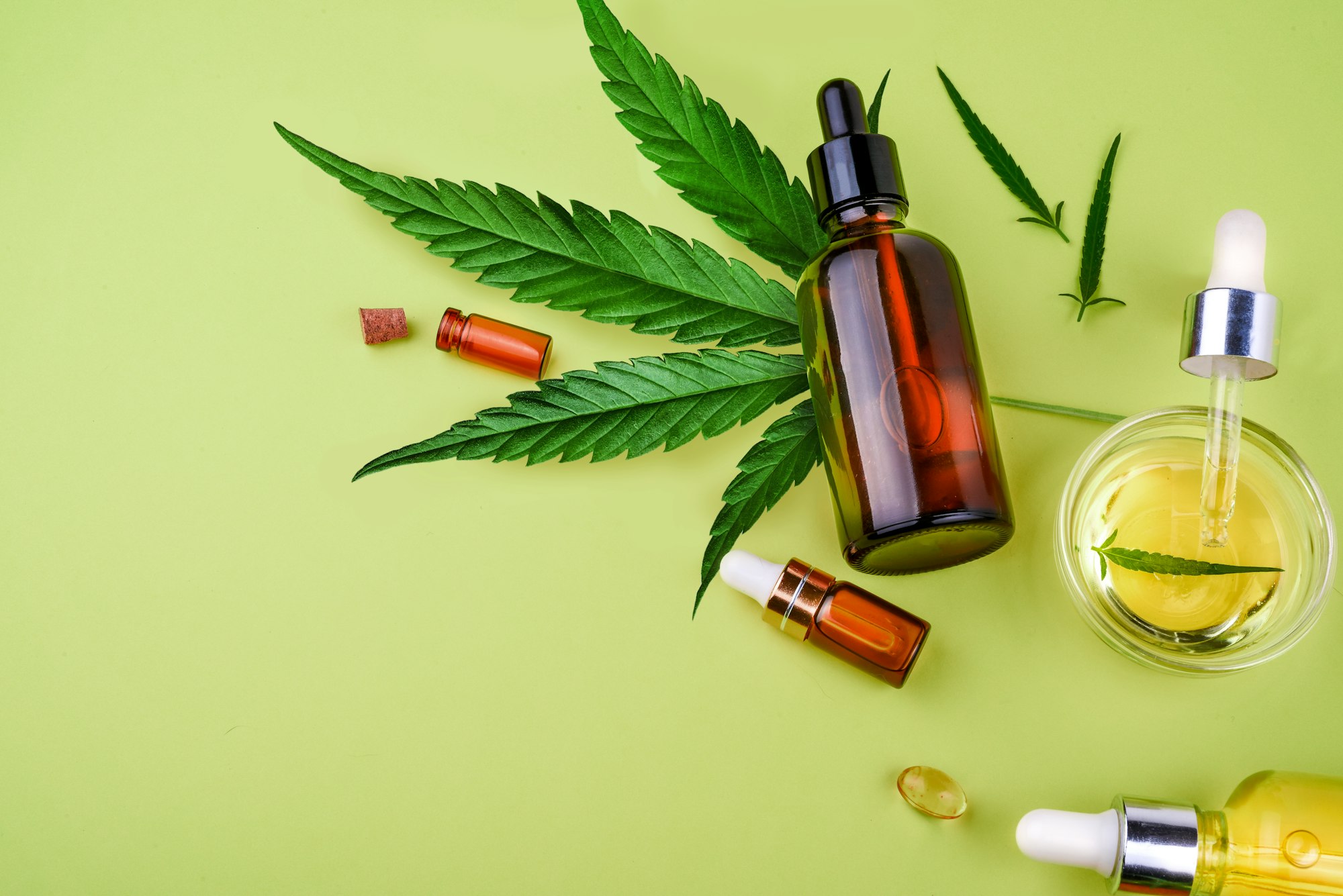 Glass bottles with CBD oil, THC tincture hemp leaves on a yellow background Cosmetics CBD hemp oil.