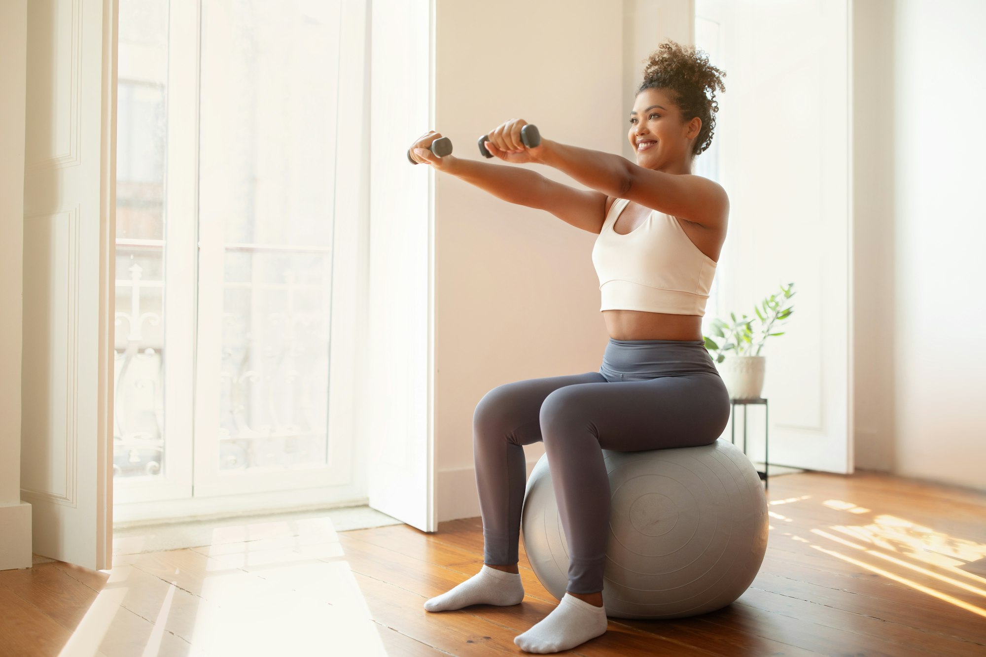 lady performs arm workout holding dumbbells using balance ball indoor