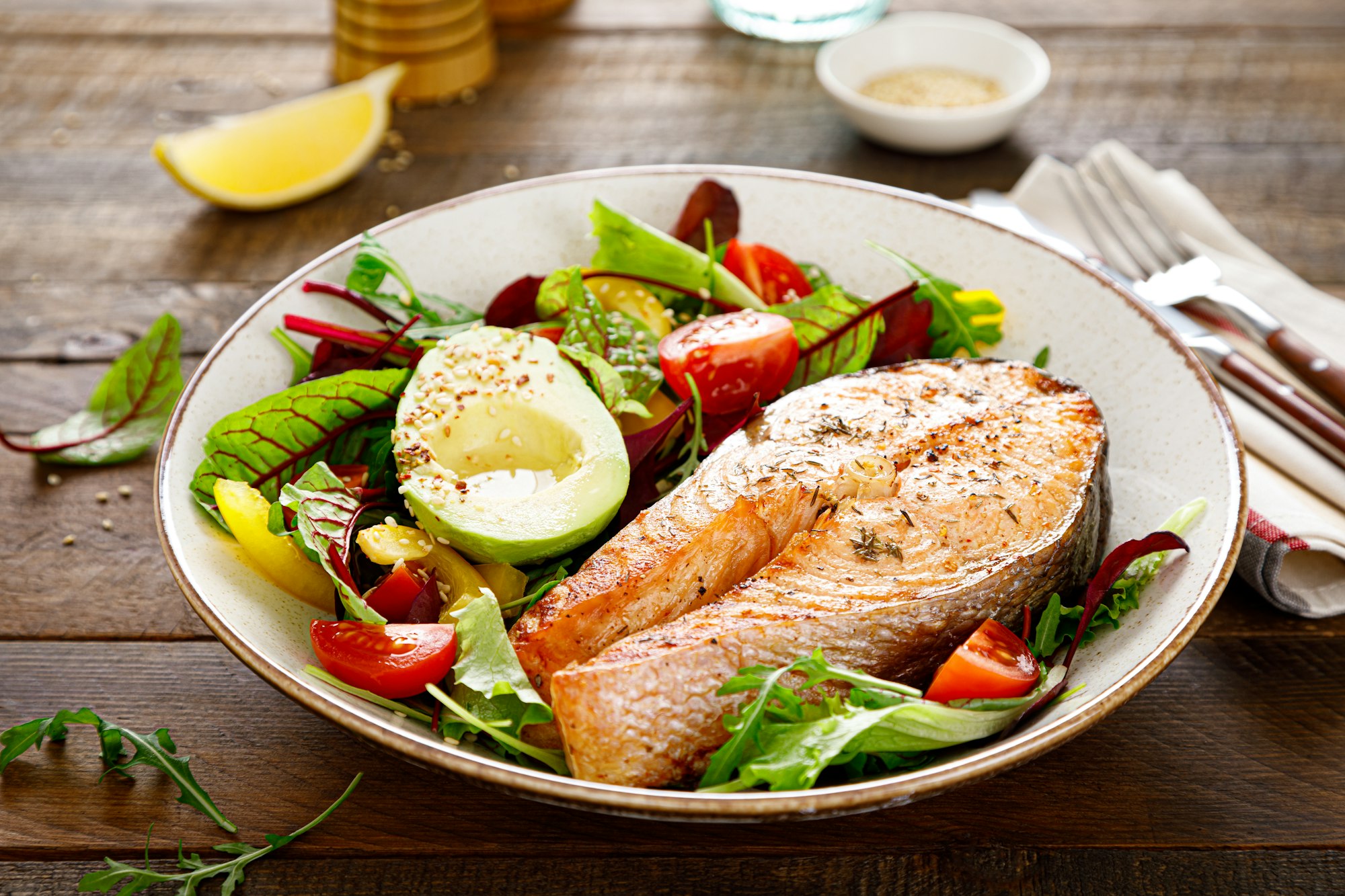 Salmon fish steak grilled, avocado and fresh vegetable salad with tomato