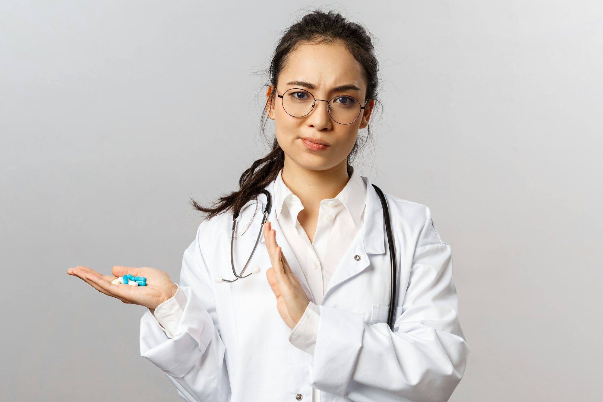 Portrait of displeased, serious-looking asian female doctor smirk skeptical, holding drugs, dont