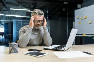 Tension headache at work. A man sits in the office, feels a headache, holds his head with his hands