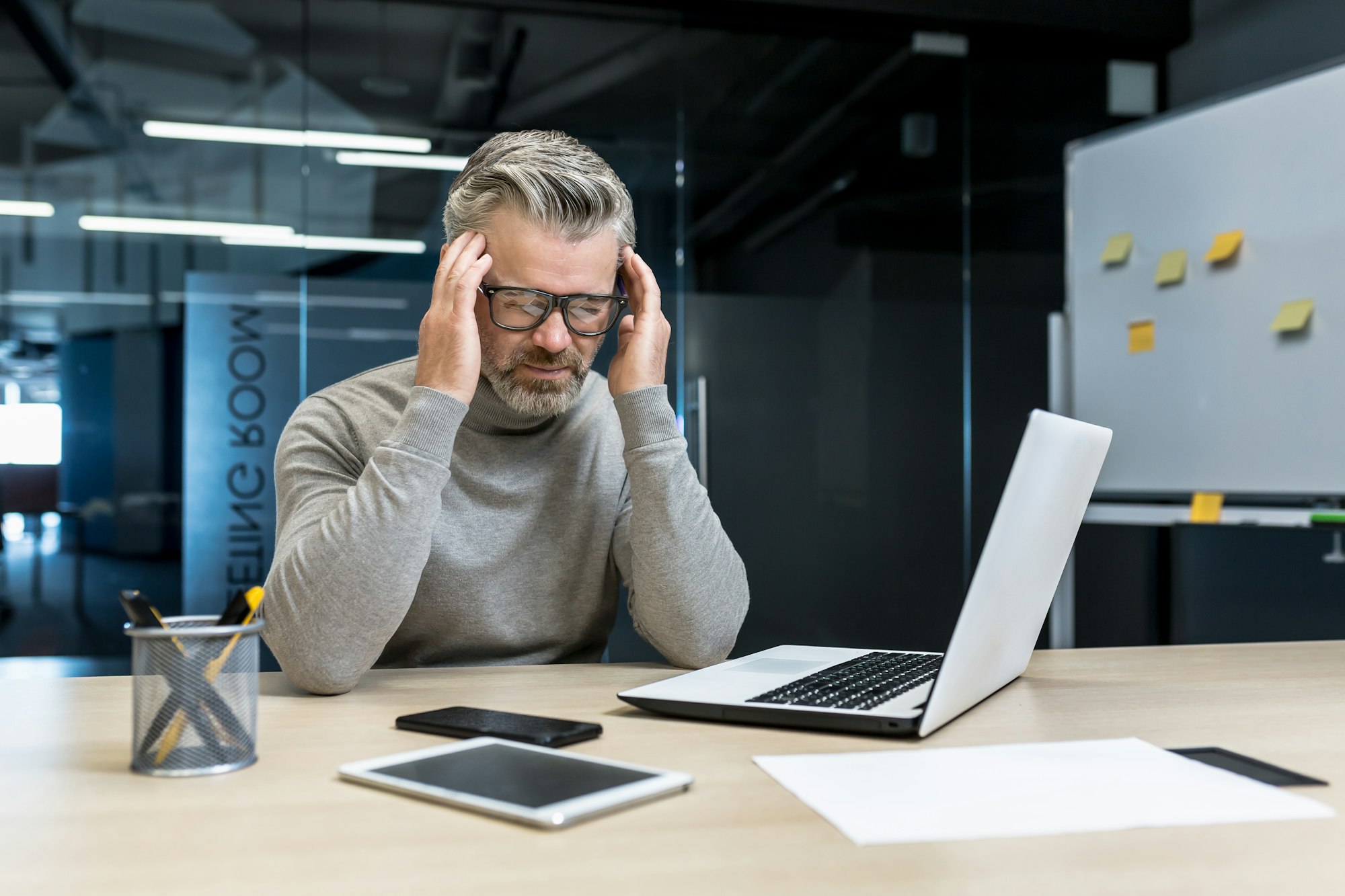 Tension headache at work. A man sits in the office, feels a headache, holds his head with his hands