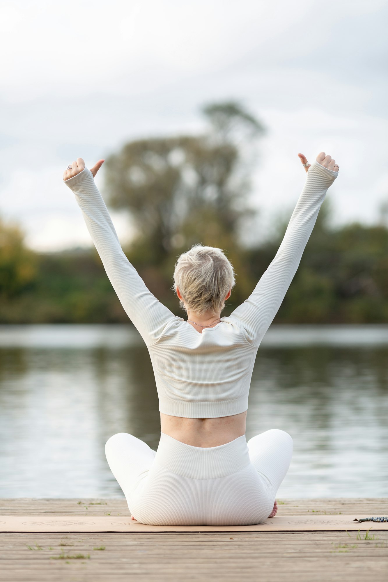 An adult woman does Kundalini yoga on a wooden pier by the river, practice of raising energy levels