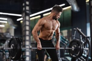 Strong weightlifter working out with heavy barbell in gym