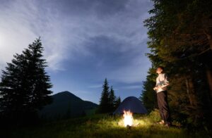 Young man is standing by a burning fire under evening sky with manifesting stars