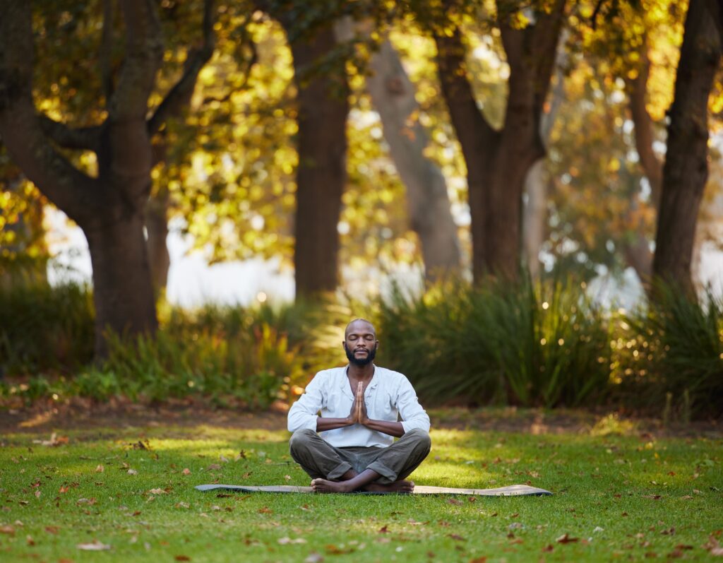 Full length shot of a handsome young man meditating while practicing yoga outside at the park