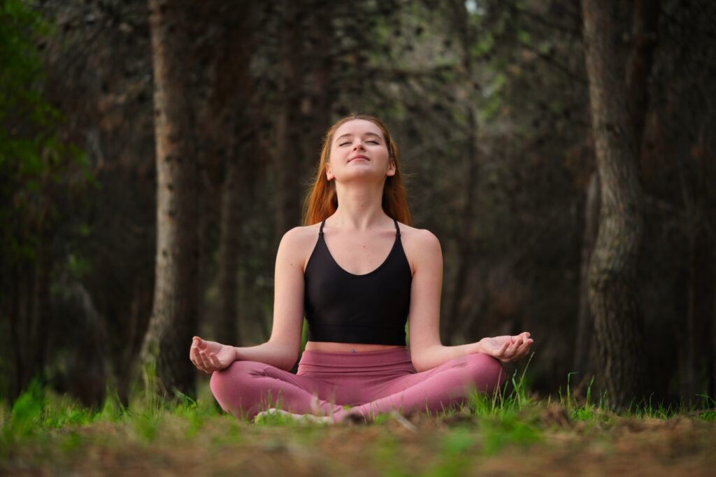 Redhead young woman meditating in a forest.
